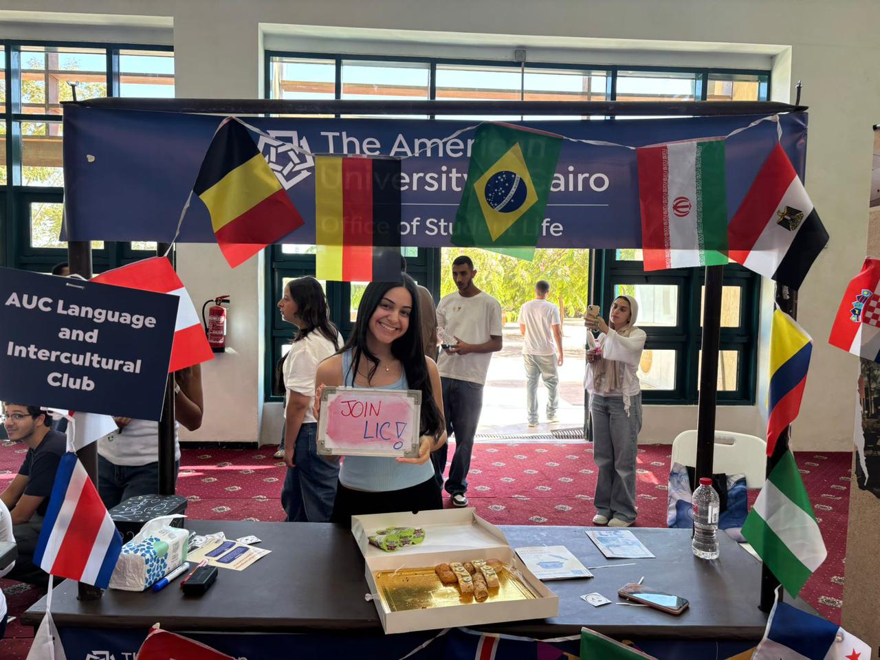 LIC member holding a JOIN LIC sign at the booth surrounded by international flags